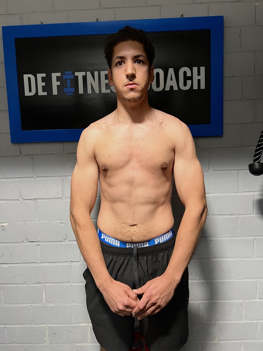 Dezelfde cliënt na het traject, poserend voor het bord van De Fitnesscoach